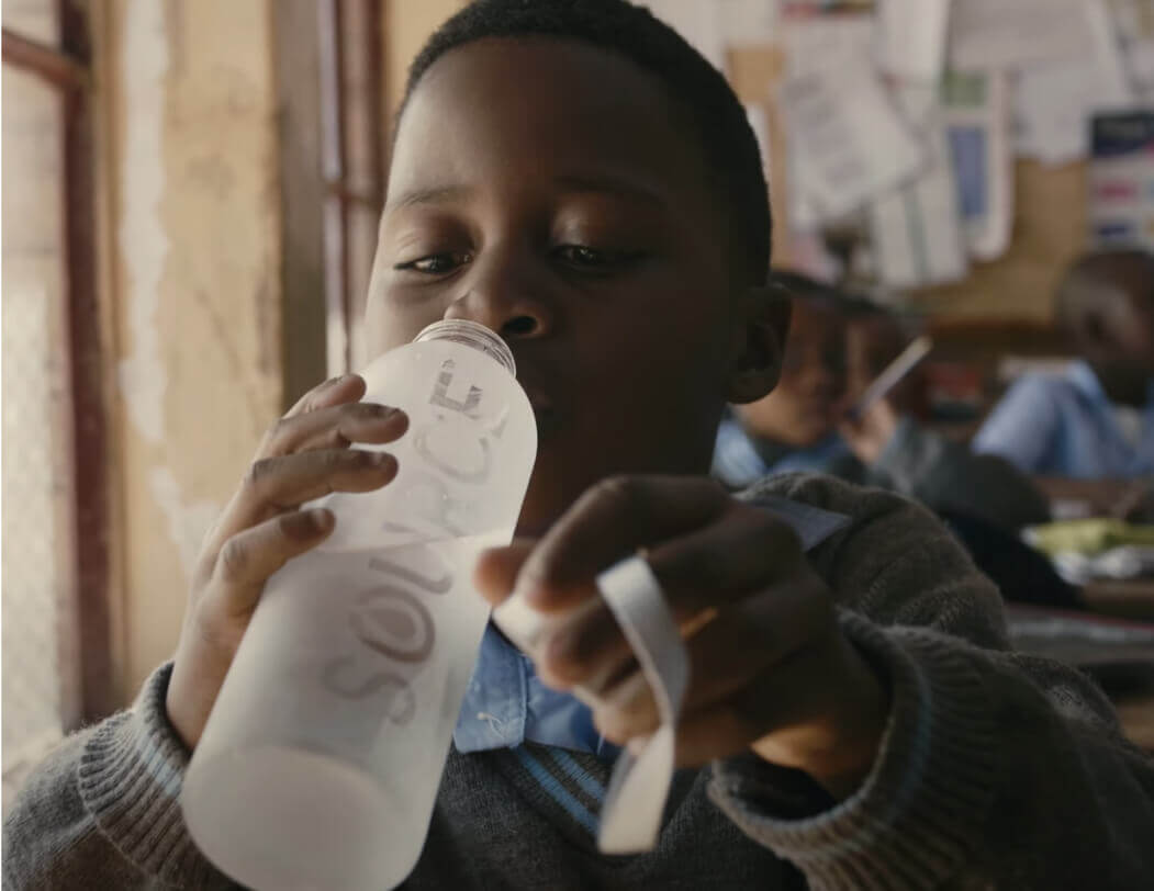 Niño bebiendo agua embotellada en la escuela con el logotipo de source meta 3